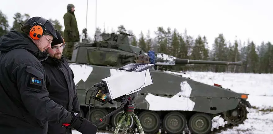 En forskare och en militär framför ett pansarfordon