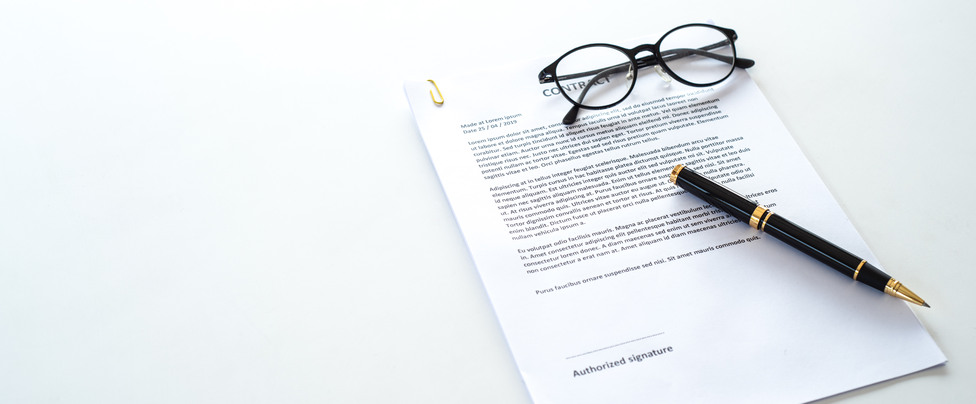 White table with paper contract detail and empty space to sign authorized signature, props with glasses and ink pen, copy space on the left